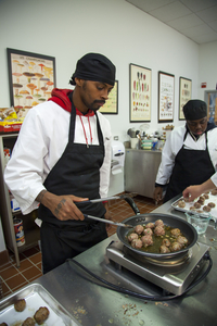 Young man of color wearing a black apron frying meatballs in a commercial kitchen.