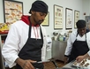 Young man of color wearing a black apron frying meatballs in a commercial kitchen.
